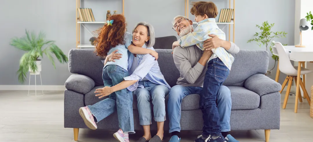 Nietos abrazando a los abuelos sentados en el sofá de la casa