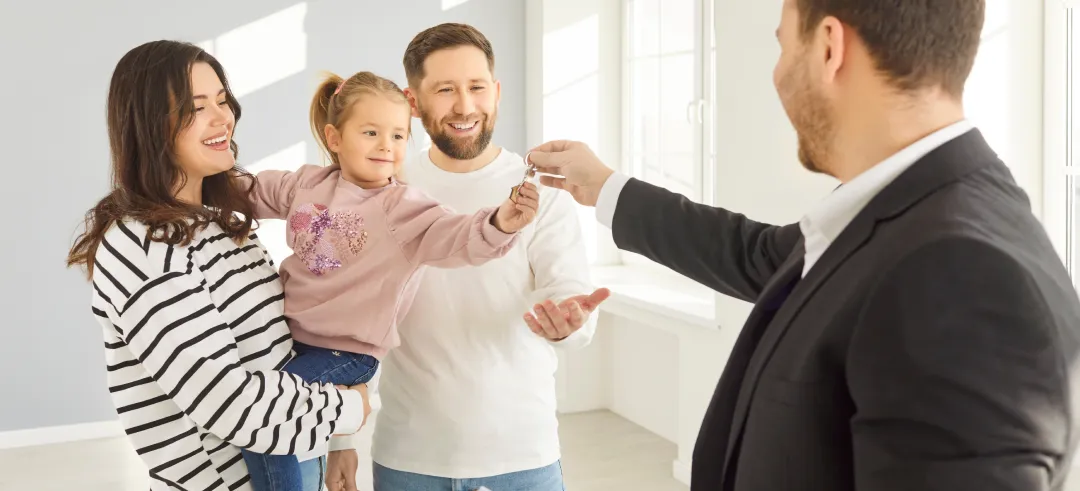Niña en brazos de su madre cogiendo las llaves de una casa con su padre al lado