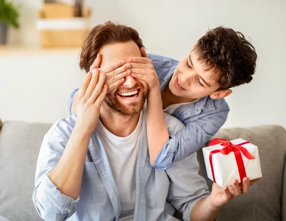 Niño tapando los ojos a su padre mientras sostiene un regalo
